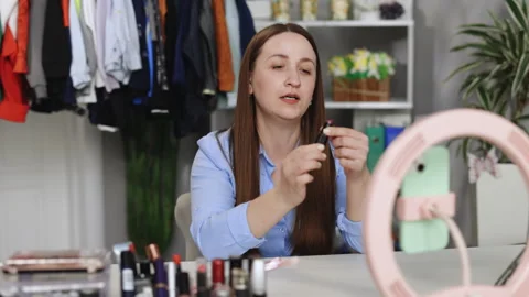 Young woman filming makeup tutorial in front of camera at home. Blogging And Stock Footage 242576865