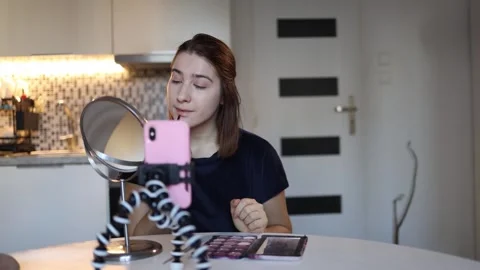Young woman films makeup tutorial on smartphone at home Stock Footage 328042944