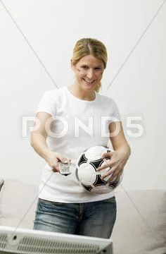 Young woman with football & remote standing in front of TV Stock Photos
