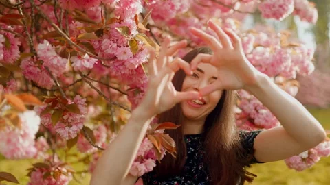 A young woman forms a heart shape with her fingers and smiles warmly Stock Footage 307289293