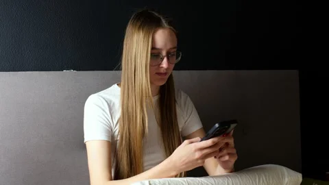 Young woman with glasses smiling while using smartphone in bed Vidéo 335367790