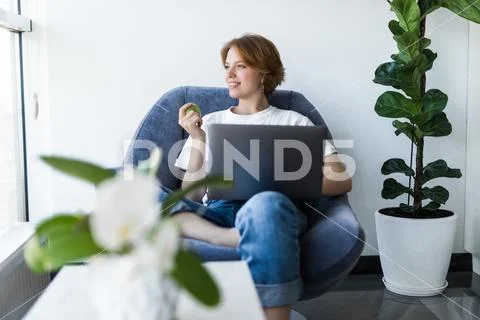 Young woman with green apple and laptop sitting in the kitchen Stock Photos