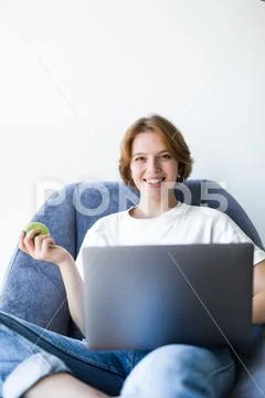 Young woman with green apple and laptop sitting in the kitchen Stock Photos