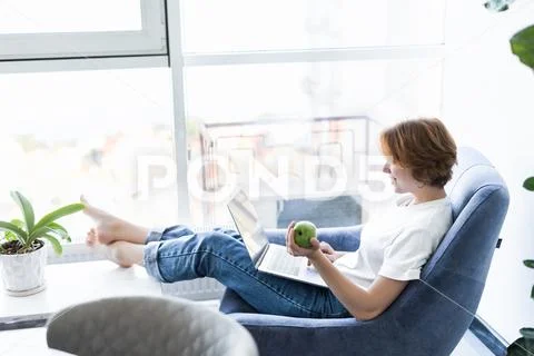Young woman with green apple and laptop sitting in the kitchen Stock Photos