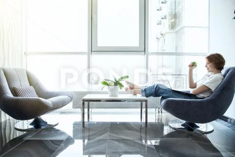 Young woman with green apple and laptop sitting in the kitchen Stock Photos