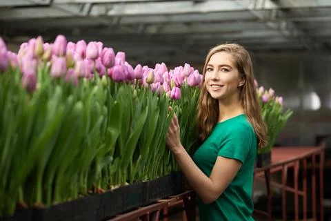 Young woman in a green dress posing at flowers in a greenhouse Tulips Stock Photos