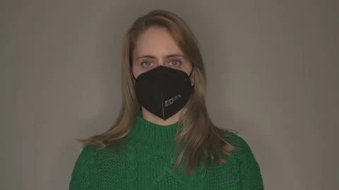Young woman in green pullover taking off black face mask in front of grey wall Stock Footage 146697562