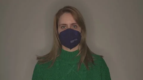 Young woman in green pullover taking off face mask in front of grey wall Stock Footage 146697596