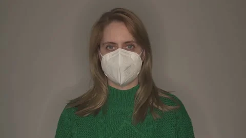 Young woman in green pullover taking off face mask in front of grey wall Stock Footage 146697619