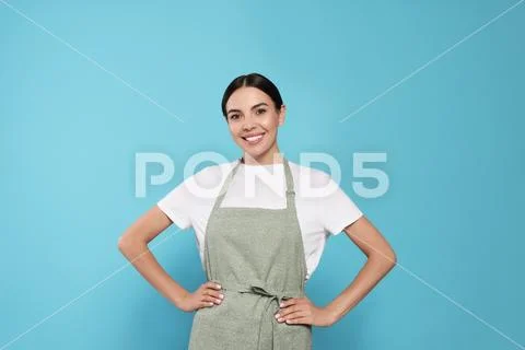 Photograph: Young woman in grey apron on light blue background, #231846912