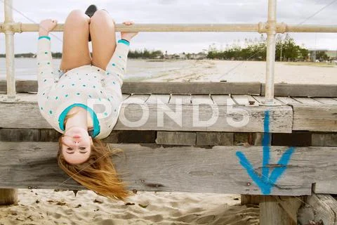 Young Woman Hanging Upside Down From Pier