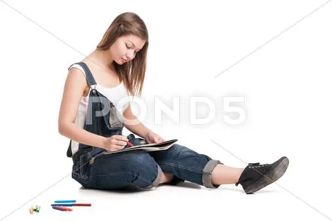 Young woman happily sitting on the floor drawing in her note pad Stock Photos