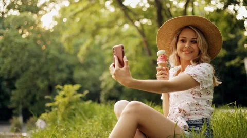 Young  woman in a hat eats ice cream and takes a selfie with a mobile phone Stock Footage 242597361