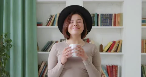 A young woman in a hat takes a sip from a mug, drinks coffe Stock Footage 130854953