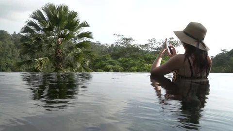 Young woman in a hat using a smartphone in the pool in the jungle. Stock Footage 104494250