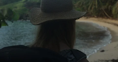 Young woman with hat walking down tropical beach alone during sunrise Stock Footage 86107781