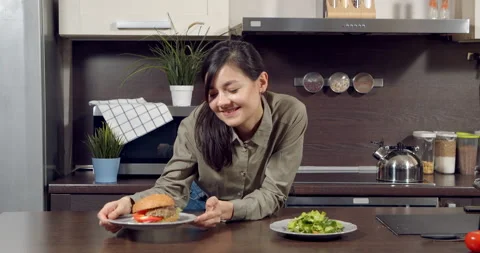 Young woman having difficulty choosing between green salad and burger and Stock Footage 150155873