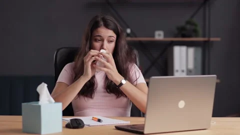 Young woman having a flu and sneezing. Woman at workplace coughs and wipes her Stock Footage