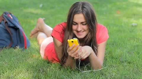 Young woman having fun using mobile cell phone lying on green grass in park HD Video stock 45417089