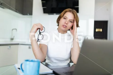 Young woman having headache while working on laptop sitting at her kitchen ta Stock Photos