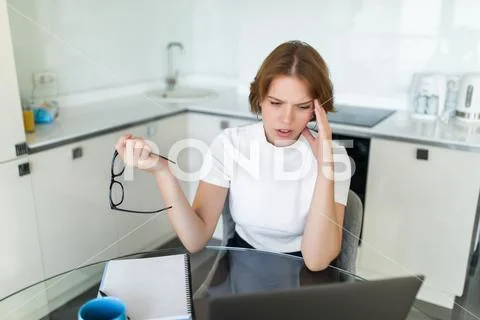 Young woman having headache while working on laptop sitting at her kitchen ta Stock Photos