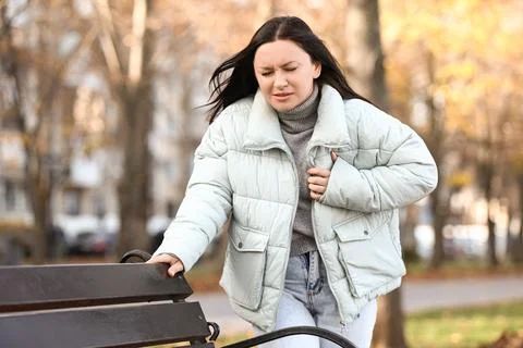Young woman having heart attack near bench in park Stock Photos