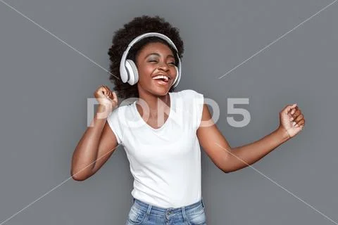 Young woman in headphones dancing isolated on gray listening music laughing Stock Photos