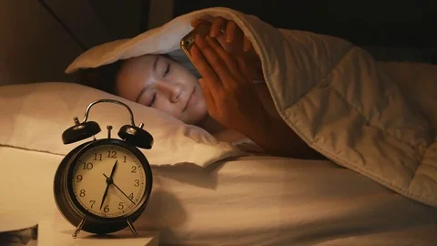 Young woman in her bed using a smartphone and smiling at midnight Stock Footage 76196140