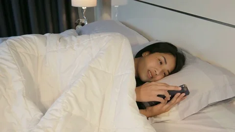 Young woman in her bed using a smartphone and smiling Stock Footage 81283224