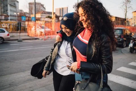 Young woman in hijab and best friend walking and talking in city Stock Photos