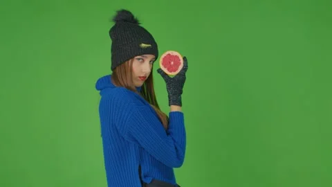 A young woman holding a grapefruit and watching at it over a green background. Stock Footage