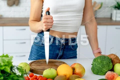Young woman holding knife while cooking fresh vegetable salad Stock Photos
