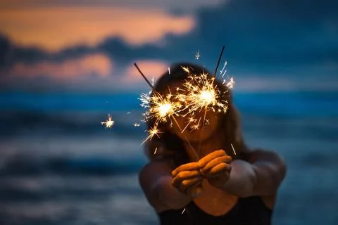 Young woman holding sparkler celebrating new years eve on the beach Stock Photos