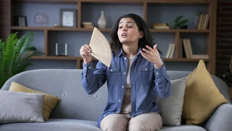Young woman is hot while sitting on the sofa in the living room at home Stock Footage 310790922