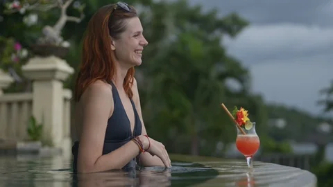 Young woman in infinity pool drinking cocktail. pretty female relax laugh smile 動画素材 124449397