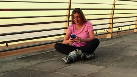 Young woman with inline skates using smartphone at sunset on the beach Stock Footage 296557253