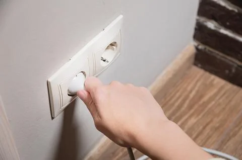 A young woman inserts a plug into a socket. A young woman plugs a charger or Stock Photos