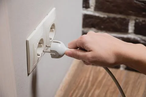 A young woman inserts a plug into a socket. A young woman plugs a charger or Stock Photos