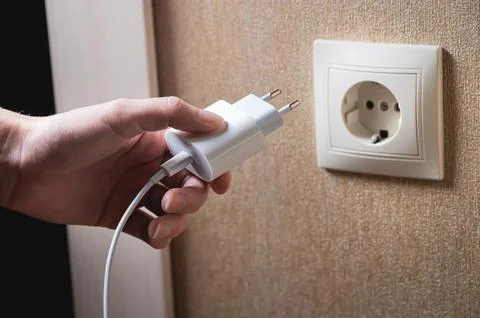 A young woman inserts a plug into a socket. A young woman plugs a charger or Stock Photos