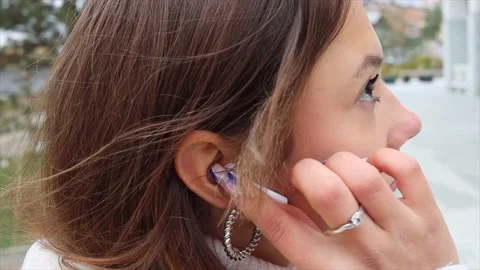 Young woman inserts a wireless white earphone into her ear close-up Stock Footage 218387042