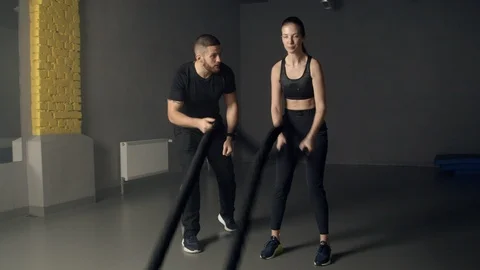 Young woman with instructor using battle ropes in gym Stock Footage 125531287