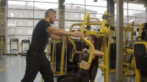 Young woman with instructor using chest press machine in gym Stock Footage 125532417