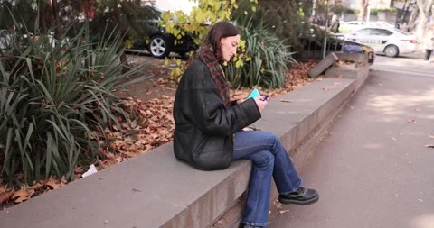 Young woman in jacket marks notes sitting on concrete parapet Vidéo 309047031