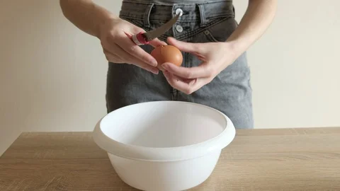 Young woman in jeans and t-shirt breaks eggs to cook Stock Footage