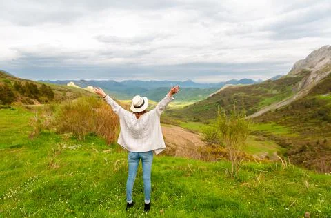 Young woman in jeans standing with hands up and open arms in the mountains Stock Photos