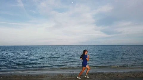 Young Woman Jogging on the Beach at Sunset. Aerial View Stock Footage