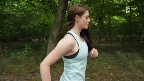 Young woman keeps looking at the camera while jogging in the forest 스톡 동영상 218272541