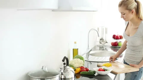 Young woman in kitchen adding fresh cut bell peppers into salad Stock Footage 25911515