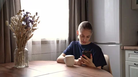 Young woman at kitchen table studying smartphone with focused worried expression Stock Footage 341554776