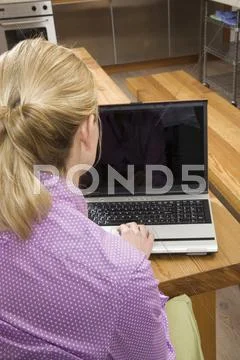 Young woman in kitchen, using laptop, rear view Stock Photos